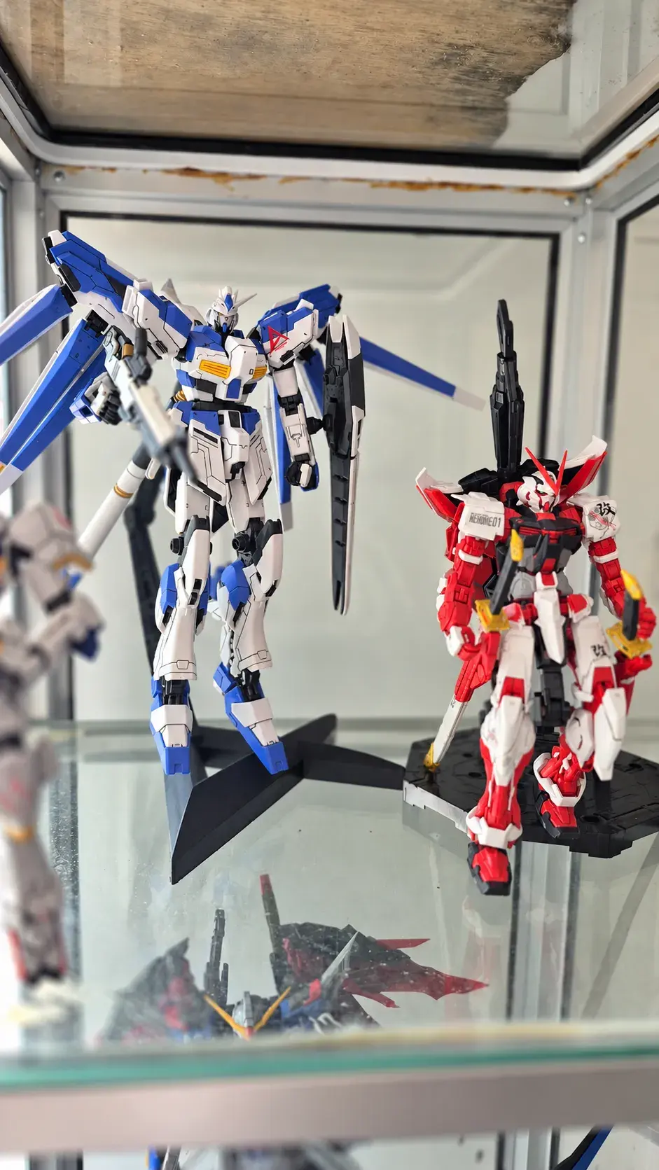 Hi-Nu Gundam and Astray Red Frame kits on a glass shelf